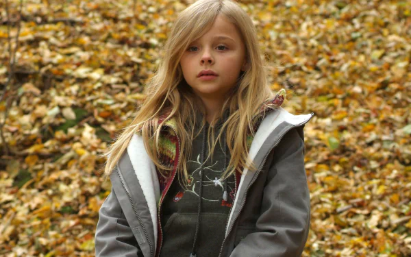 A high-definition desktop wallpaper featuring a young Chloë Grace Moretz, standing outdoors amidst a backdrop of autumn leaves.