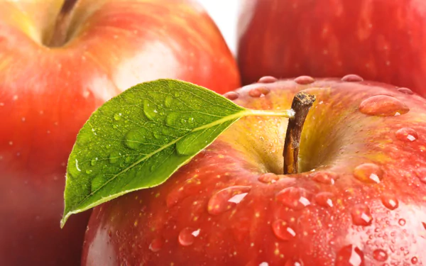 Close-up of fresh red apples with water droplets and a green leaf, captured in vibrant detail for an 8K Ultra HD PC desktop wallpaper and background.
