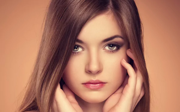HD desktop wallpaper features a woman with long brown hair, her face framed by her hands, set against a soft brown background.