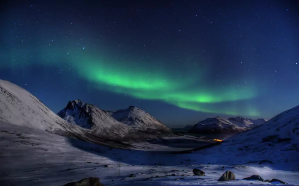 Nighttime snow-covered landscape with the aurora borealis lighting up the sky, set against a backdrop of mountains. This HD desktop wallpaper captures the natural beauty of the northern lights.