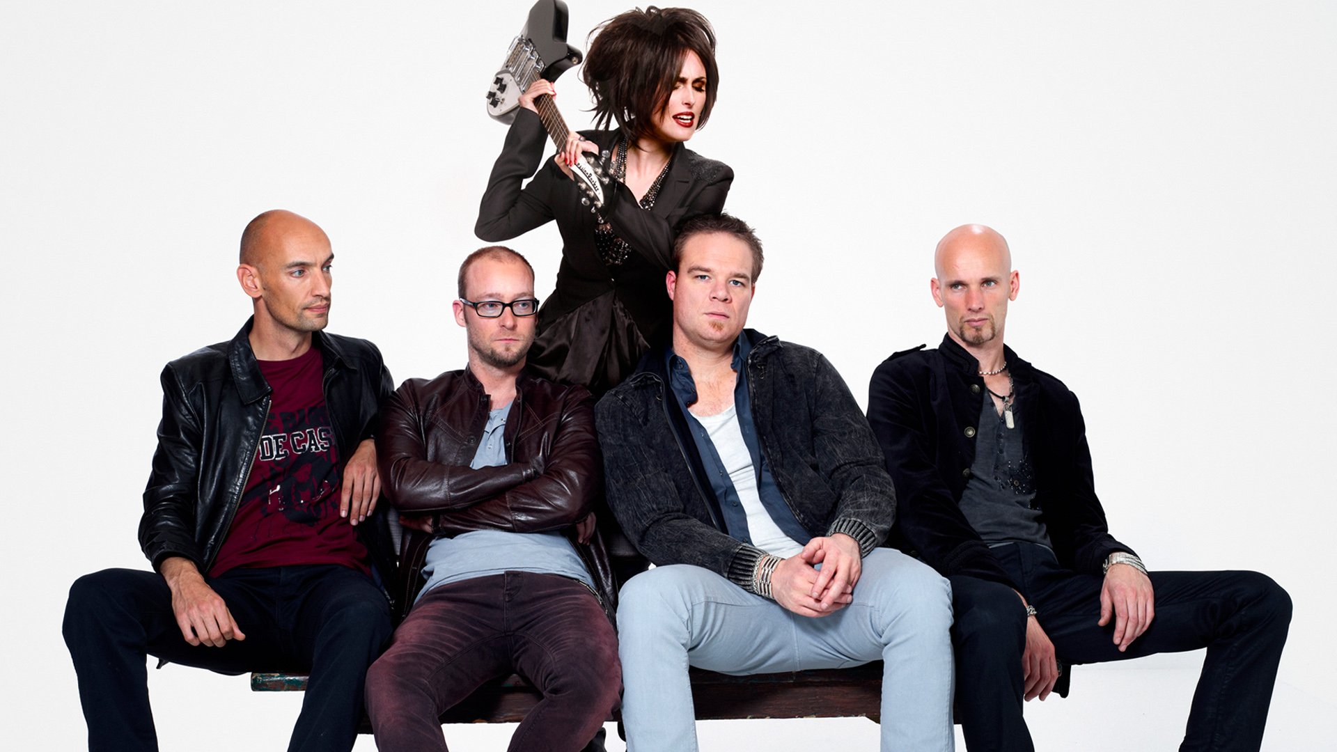HD PC wallpaper of a five-member music band: female vocalist with guitar standing behind four seated male members, all in dark stage-style clothing on a white background.