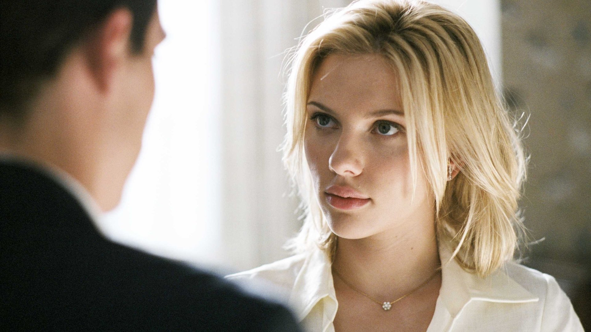 Blonde woman in a white blouse gazes at a man in the foreground in a cinematic film still — 2K Quad HD PC desktop wallpaper.