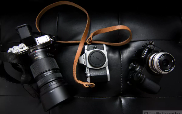 Man-made arrangement of three cameras and lenses on black leather, a 5K Ultra HD PC desktop wallpaper and background showcasing vintage and modern camera gear.