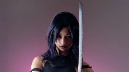A confident woman in cosplay, wielding a sword, poses against a gradient background. This striking image serves as an HD desktop wallpaper and background.