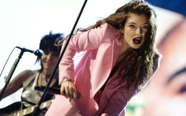 HD PC desktop wallpaper: music-themed portrait of a female singer in a pink suit mid-performance — a Lorde-inspired stage image.