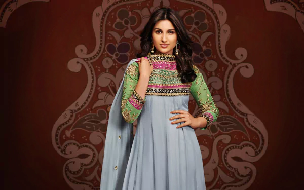 Brunette woman in an embroidered anarkali with sheer green sleeves posed before an ornate maroon motif — Bollywood-style HD PC desktop wallpaper.