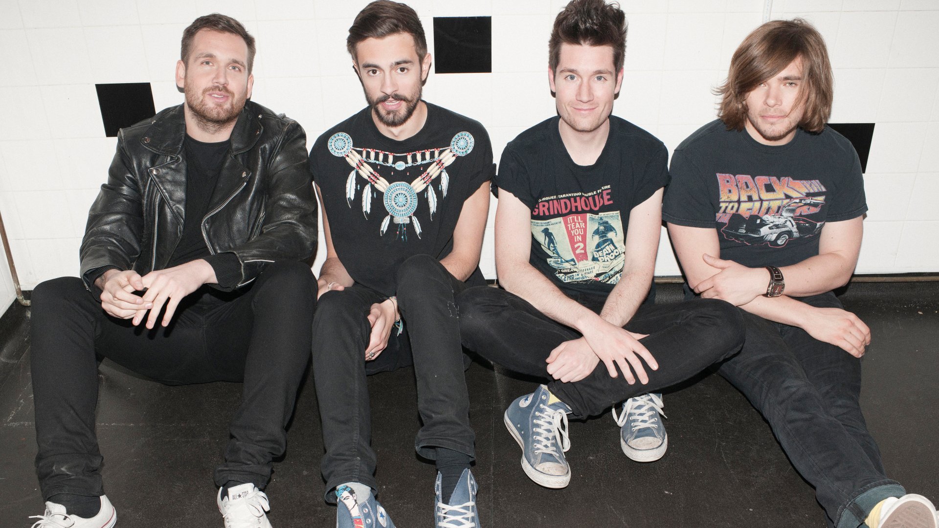 Portrait of the English rock band Bastille sitting together, featured in a 4K Ultra HD PC desktop wallpaper celebrating their music.