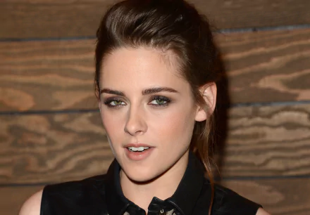 A high-definition desktop wallpaper featuring celebrity Kristen Stewart, captured with a stylish and confident expression against a wooden backdrop.
