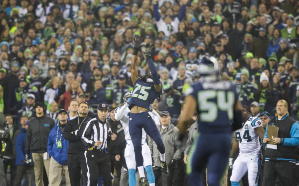Seattle Seahawks player making a leaping catch during a high-stakes playoff game, with a packed stadium crowd in the background.