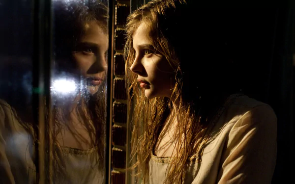 A captivating HD wallpaper featuring Chloë Grace Moretz in a dramatic scene from the movie Let Me In, reflecting an intense moment with her image mirrored beside her.