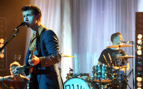 HD desktop wallpaper featuring the English rock band Arctic Monkeys performing live with a guitarist and drummer on stage.