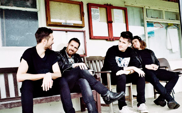 HD desktop wallpaper of the English rock band Bastille, featuring the four members sitting and interacting casually outside a building.