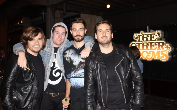 HD desktop wallpaper featuring the English rock band Bastille posing together with The Other Rooms sign illuminated in the background.