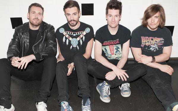 Portrait of the English rock band Bastille sitting together, featured in a 4K Ultra HD PC desktop wallpaper celebrating their music.