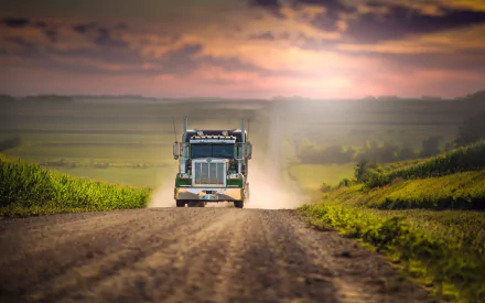 A powerful truck drives along a dusty road, framed by lush greenery and a dramatic sunset, creating a vivid HD desktop wallpaper and background.