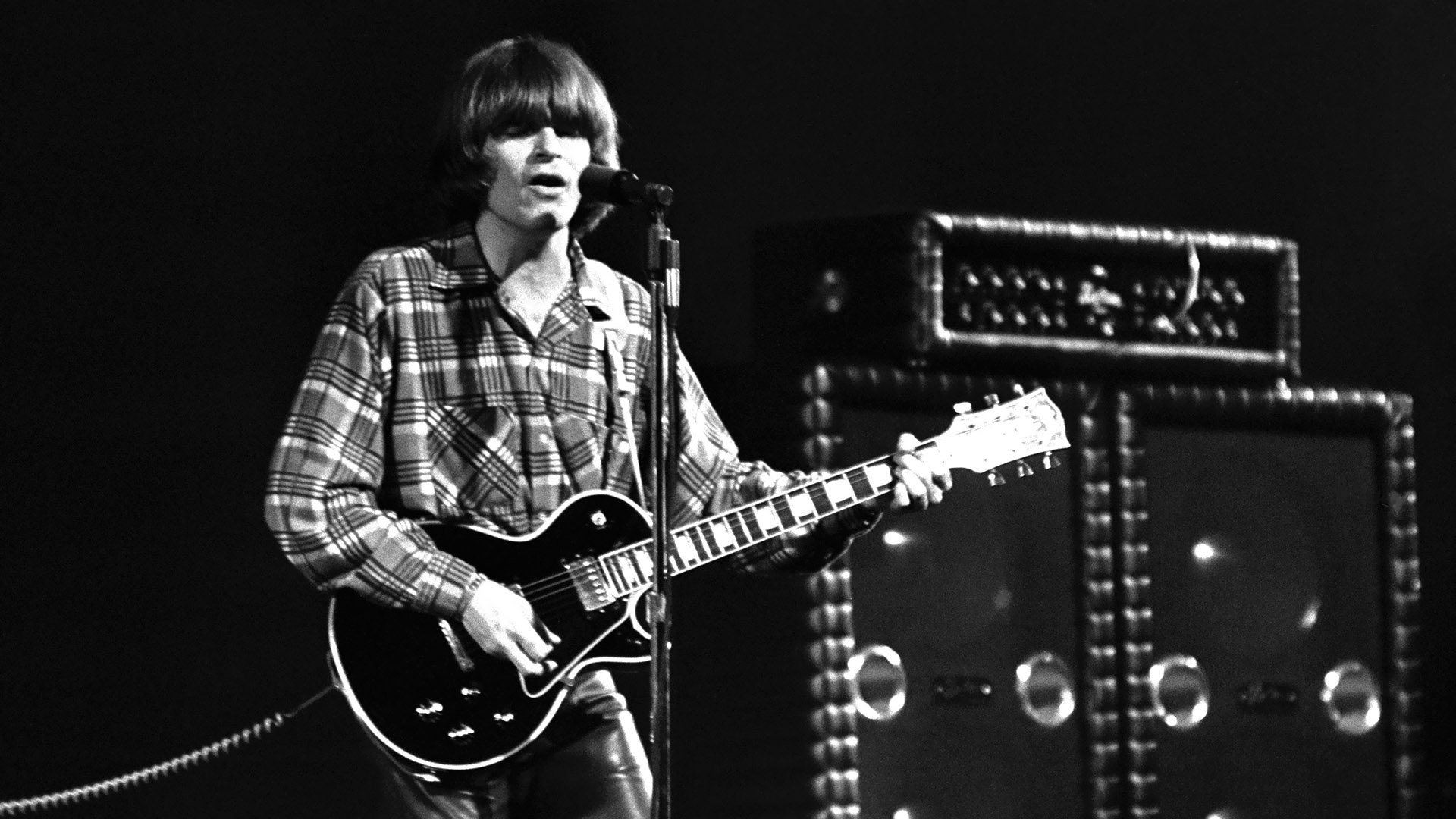 Black and white HD desktop wallpaper showing a Creedence Clearwater Revival musician playing guitar and singing on stage.