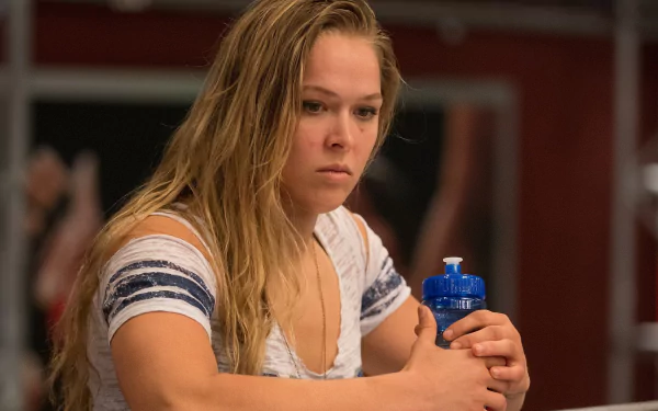 Ronda Rousey is depicted in a contemplative moment, holding a water bottle, showcasing the intensity and focus of an elite athlete in this HD desktop wallpaper.