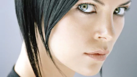 HD PC desktop wallpaper of the movie Aeon Flux character: close-up of a pale face with intense green eyes, short black hair and a minimalist gray background.