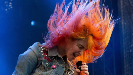 HD desktop wallpaper of Hayley Williams passionately singing on stage with vibrant orange hair flying, capturing an intense music performance moment.