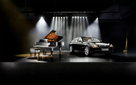 A sleek black BMW 7 Series car and a Steinway grand piano are showcased side by side under bright stage lights in a dark, dramatic setting.