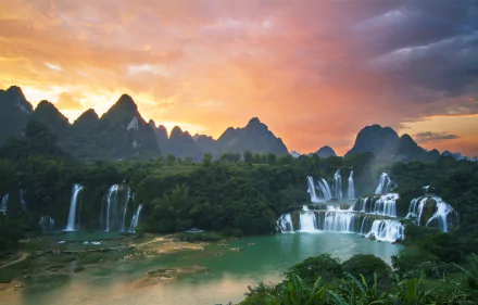 Sunset over Ban Gioc-Detian Falls on the Quây Sơn River, with lush mountains and vibrant skies in Vietnam's natural landscape.