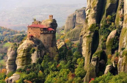 A stunning HD desktop wallpaper of a historic monastery perched atop cliffs in Meteora, Greece, surrounded by lush greenery and rocky formations.