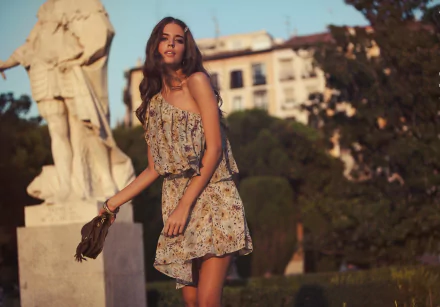 A woman in a floral dress holds a bag, posing outdoors near a statue, with buildings and greenery in the background. This image is tagged with Clara Alonso and is an HD desktop wallpaper and background.