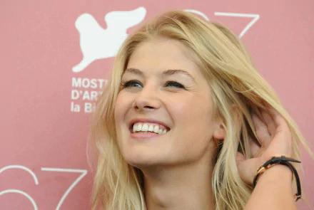 HD wallpaper of Rosamund Pike smiling with a pink background. Suitable as a desktop background.