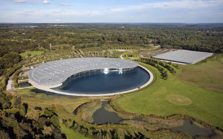 2K Quad HD desktop wallpaper: aerial view of McLaren Technology Centre, a man-made curved building with reflecting pool set in a green landscape.