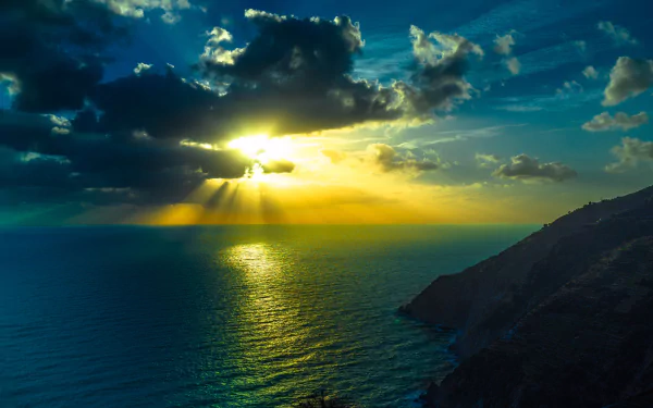 HD desktop wallpaper featuring a stunning ocean sunset with sunbeams breaking through clouds, casting a warm glow over the sea, and illuminating the natural scenery.