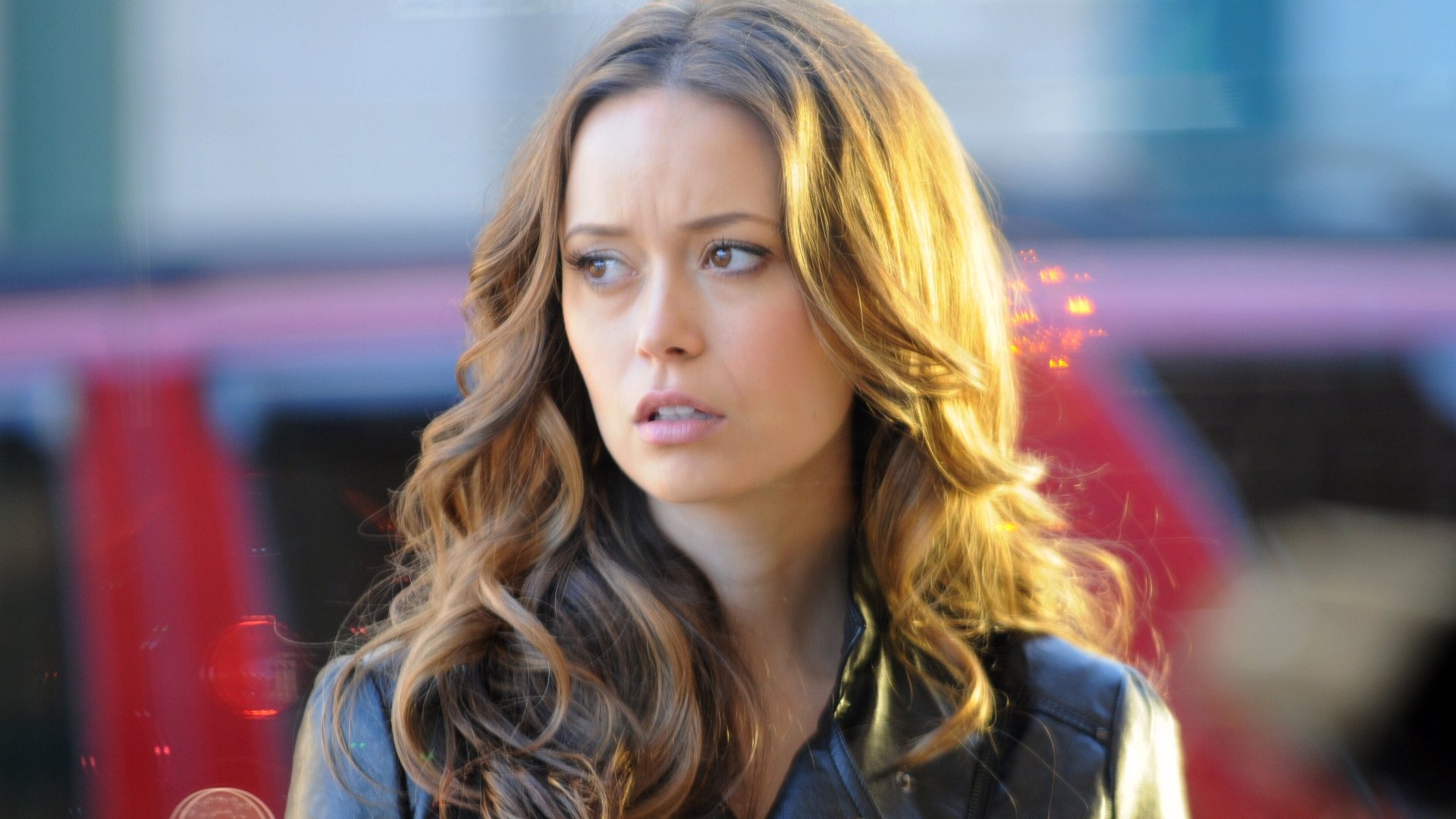 Close-up portrait of a female celebrity with long wavy brown hair, contemplative gaze and warm rim light. 4K Ultra HD PC desktop wallpaper/background.