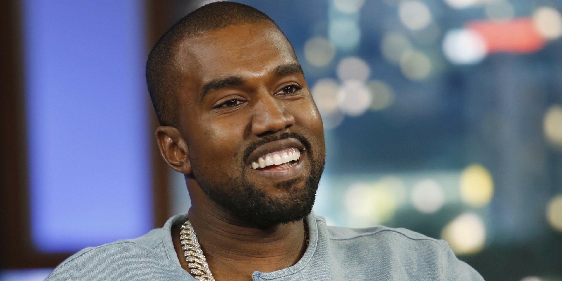 HD desktop wallpaper featuring a smiling man in a grey shirt with a blurred background.