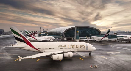 HD desktop wallpaper of Emirates Airbus A380 airplanes at an airport, with a modern terminal building and a dramatic cloudy sky in the background.