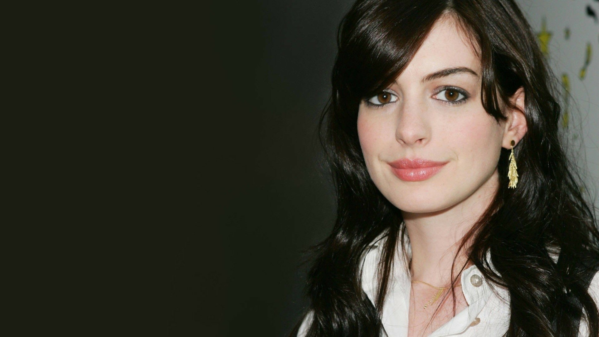 HD desktop wallpaper of Anne Hathaway wearing gold earrings, showcasing her face with dark hair against a dark background.