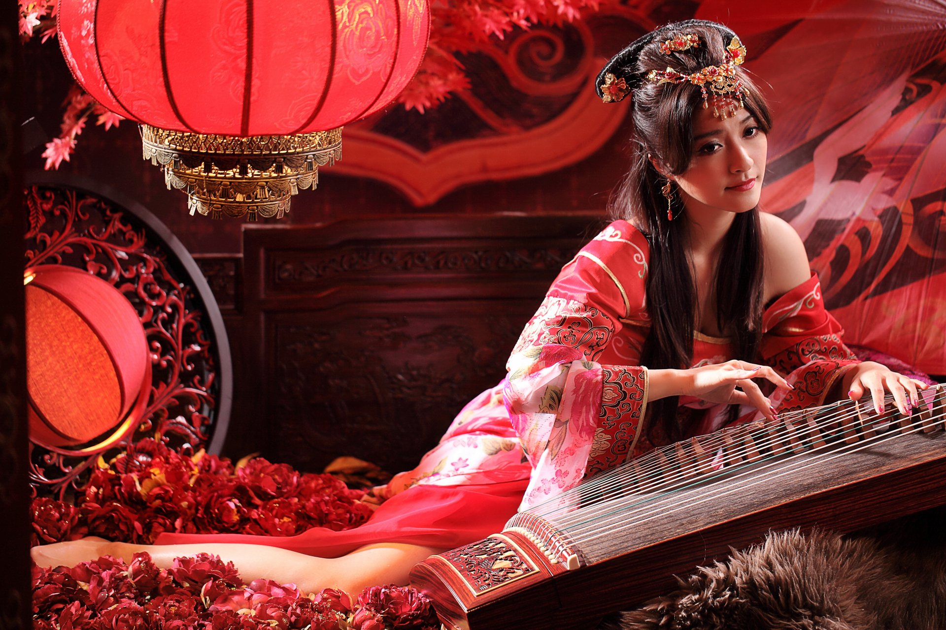 A woman in traditional Asian dress poses with a zither, surrounded by red lanterns and floral decor, creating an enchanting atmosphere in this vibrant 4K Ultra HD wallpaper.