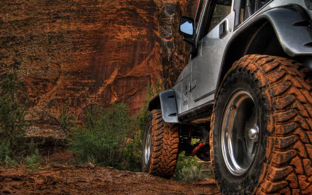 A rugged Jeep parked on a dirt path, showcasing its powerful tires against a dramatic red rock backdrop, featured as a striking HD desktop wallpaper.