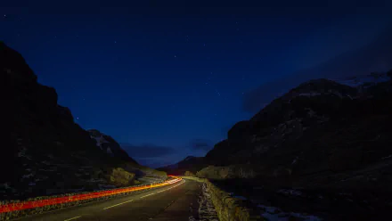 Night starry sky over Snowdonia with a winding man-made road lit by vehicle light trails — 5K Ultra HD PC desktop wallpaper/background.