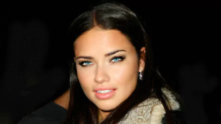 HD PC desktop wallpaper featuring a close-up portrait of celebrity Adriana Lima with striking blue eyes and dark hair against a black background.