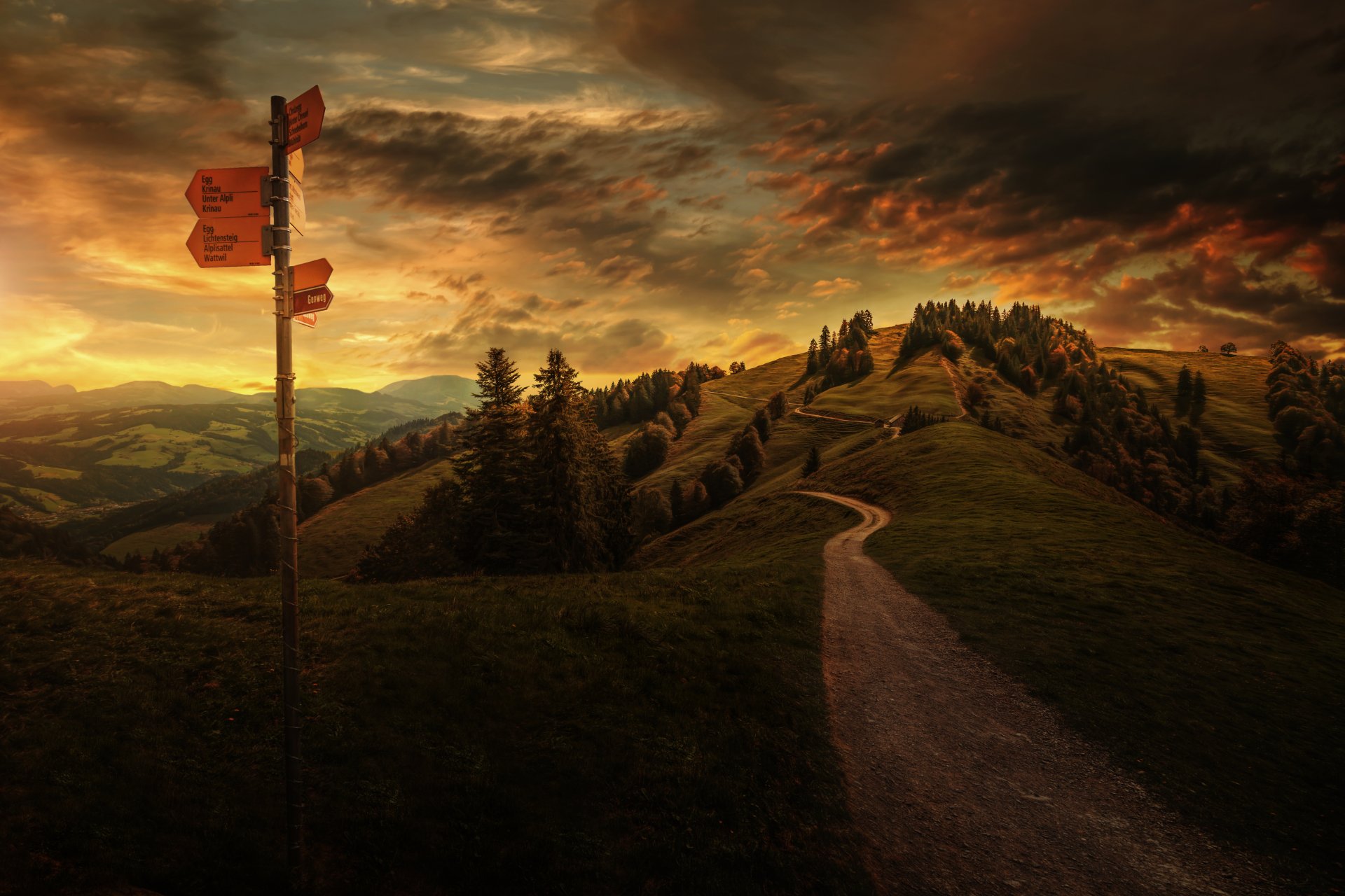 Dramatic sunset over a winding path on a hill in the Swiss countryside, surrounded by trees under a vibrant cloudy sky, captured in 4K Ultra HD landscape photography.