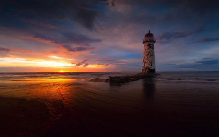 A dramatic sunset casts vibrant colors over a serene beach, highlighting a weathered lighthouse standing resilient against the tranquil waters, creating a captivating landscape scene.
