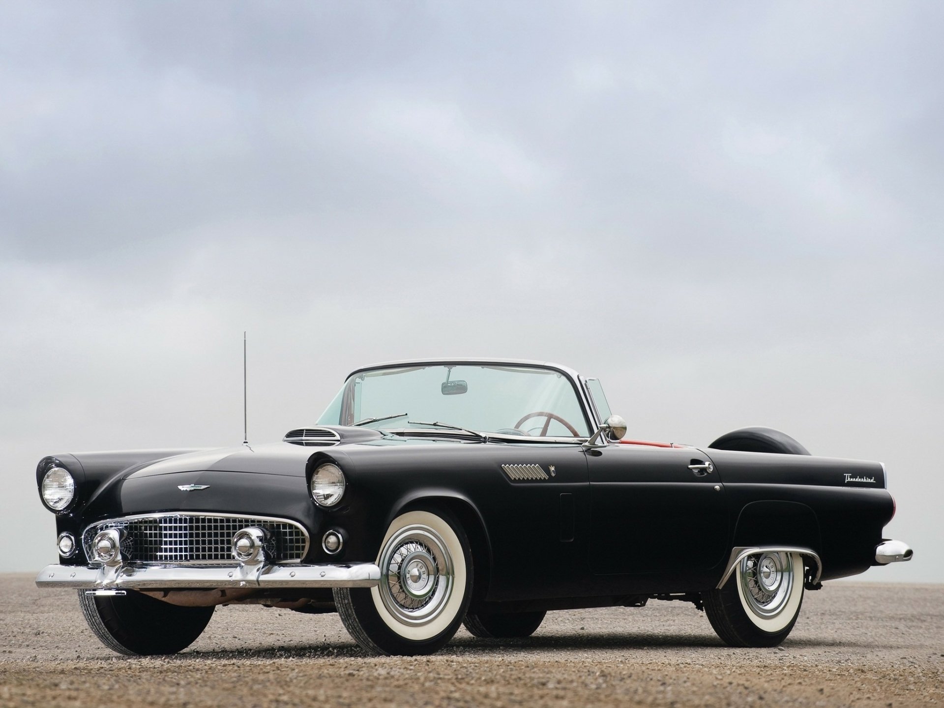 Black classic Ford Thunderbird convertible on open pavement under an overcast sky — HD PC desktop wallpaper background featuring the vehicle.