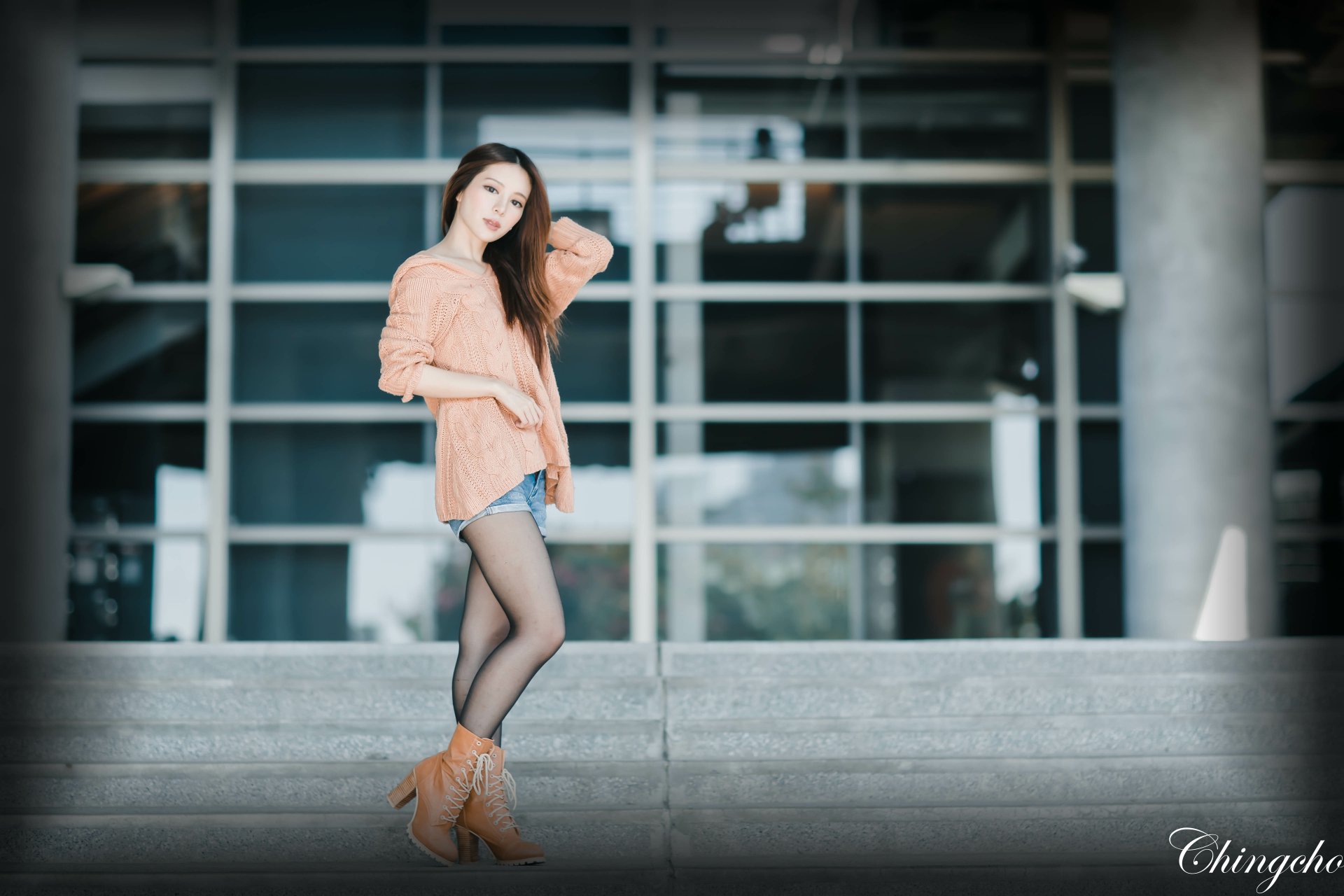 A Taiwanese woman, Julie Chang, poses confidently in a peach blouse and shorts with stockings and heels in front of a modern building, captured in 4K Ultra HD.