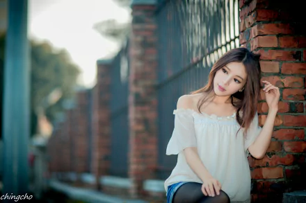 A brunette Asian model, Julie Chang, poses gracefully against a brick wall, showcasing a soft bokeh effect, creating a serene atmosphere in this 4K Ultra HD background.