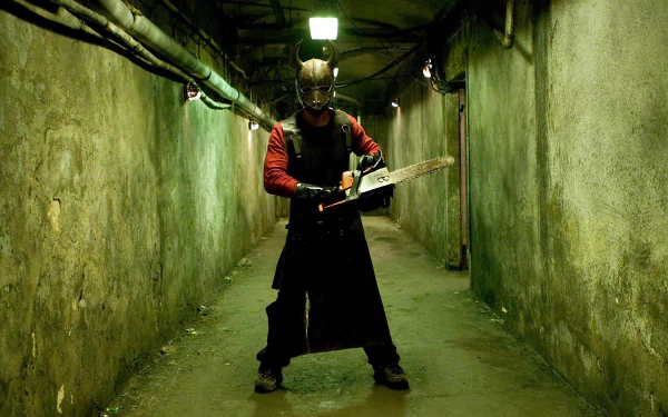 HD PC desktop wallpaper from the movie Hostel featuring a menacing figure holding a chainsaw in a dimly lit, narrow underground corridor.
