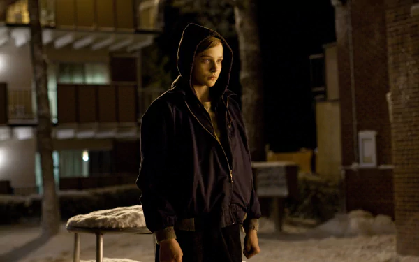Chloë Grace Moretz stands in a snowy outdoor scene from the movie Let Me In, embodying a mysterious and captivating presence in this HD desktop wallpaper.