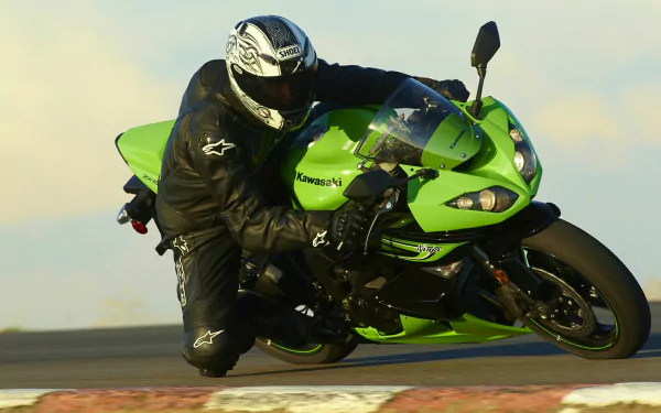 Rider leaning into a turn on a green Kawasaki sportbike vehicle on a racetrack — HD PC desktop wallpaper background.