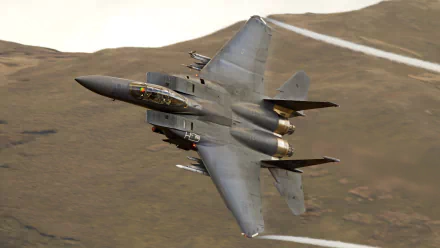 HD desktop wallpaper featuring a McDonnell Douglas F-15 Eagle military jet flying low over rugged terrain.