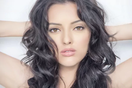 HD desktop wallpaper featuring a brunette model with wavy hair, identified as Kristina Akheeva, posing confidently with her hands behind her head and an intense gaze.