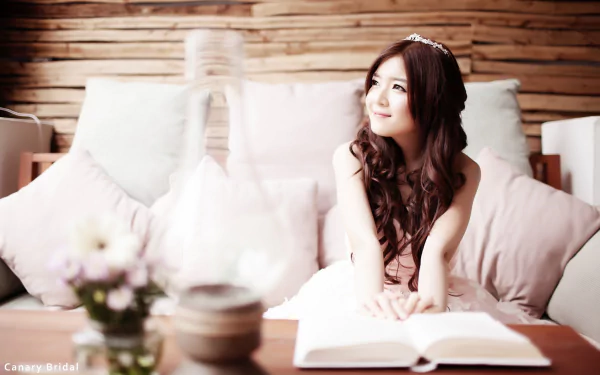HD desktop wallpaper featuring an Asian woman, tagged as a Vietnamese bride and model, sitting with a book and smiling. The setting exudes a relaxed and happy mood.