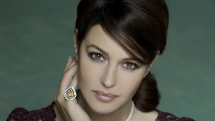 HD wallpaper featuring a brunette Italian actress and model with brown eyes, wearing a ring and gazing confidently. The background is a soft, light green that showcases her elegance.